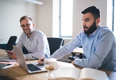 Two men sitting at a table with laptops.