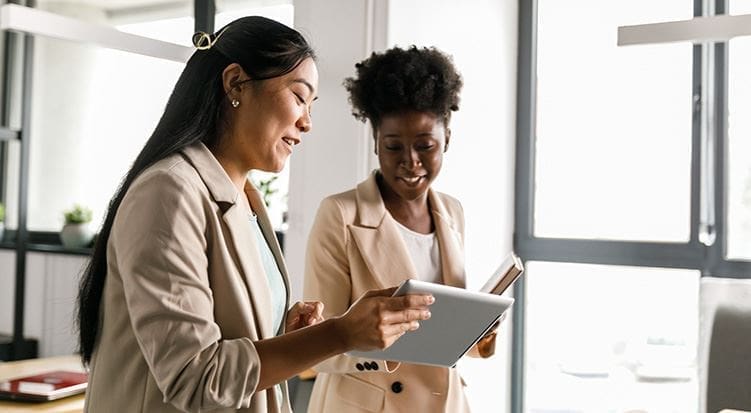 Two women are smiling while looking at a tablet.