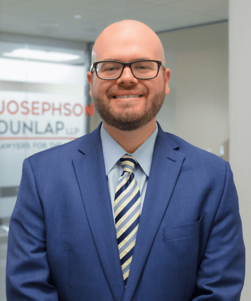 Man in blue suit and glasses smiling.