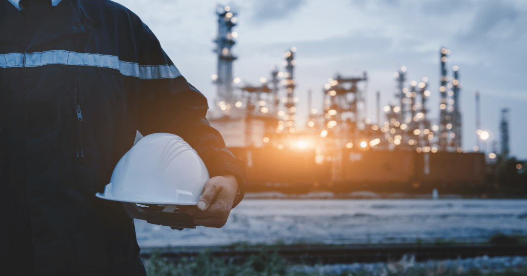 Engineer holding helmet near industrial plant.